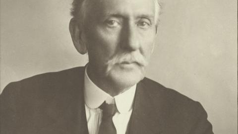 photographic portrait of Blake with a thick white mustache and black suit looking directly at the viewer in a self assured manner