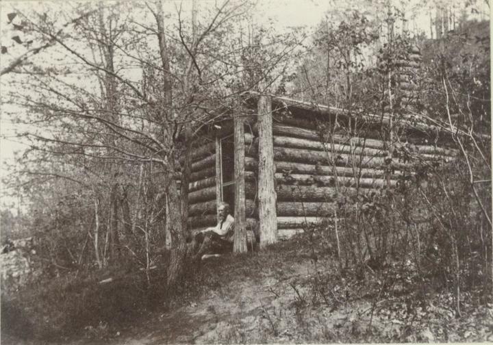 Image of Brewster sitting on front step of his small cabin in Concord, Mass.